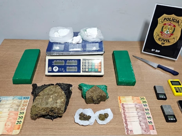 Imagem de uma mesa contendo as drogas apreendidas: tabletes de maconha e porções grandes de cocaína. Além de balança de precisão e dinheiro m espécie.